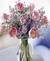 
Pastel pink tulips, combined with lovely and fragrant lavender lilacs are beautifully arranged in a simple glass urn for a take-your-breath-away taste of Spring...
			