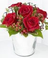 
Bursts with the shine and exuberance of the holiday season! Rich red roses sit amongst red hypericum berries, assorted holiday greens and silver glass balls, beautifully arranged in a silver metallic...
			